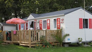 A mobile home with a wooden deck, red shutters, and a pink umbrella. - Camping Pen Guen (Saint-Cast-le-Guildo)
