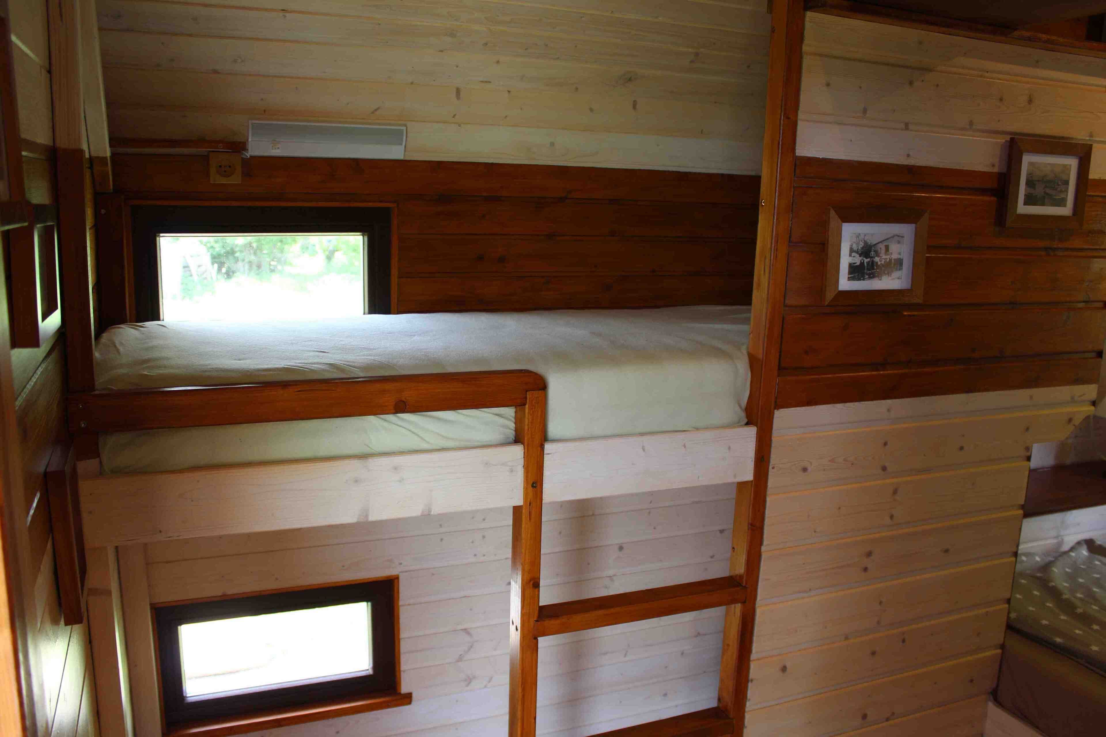 A bunk bed with a ladder, wooden walls, and a small window.