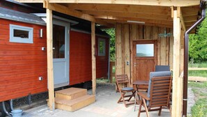 A wooden cabin with a covered patio, a dining table, and four chairs.