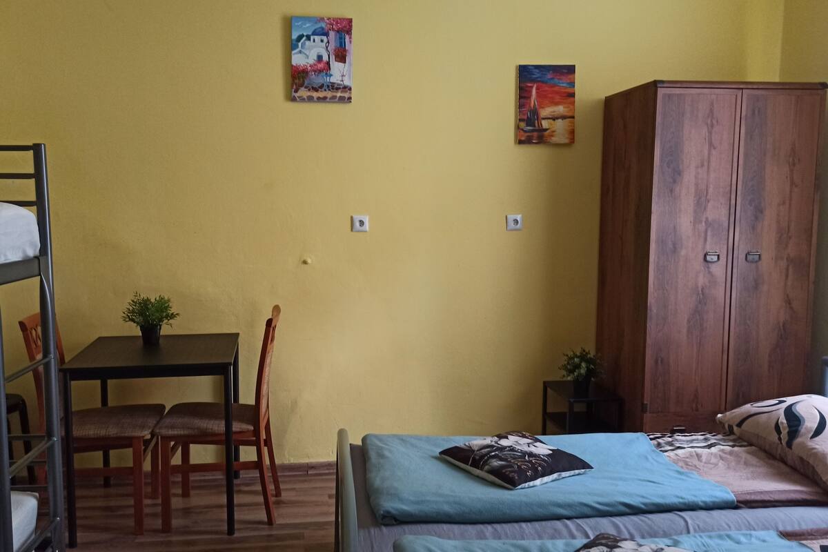 Ein Schlafraum mit Etagenbetten, einem Schreibtisch, Stühlen, einem Holzschrank und zwei Bildern an der Wand.