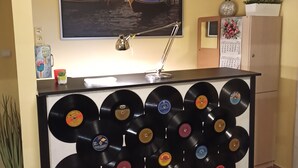 Una habitación con un estante para tocadiscos montado en la pared lleno de discos de vinilo, un cuadro de una escena de canal, un reloj y un calendario.