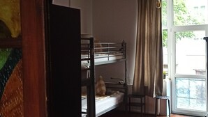 Una habitación con literas, piso de madera, ventana con cortinas y una planta sobre una mesa.