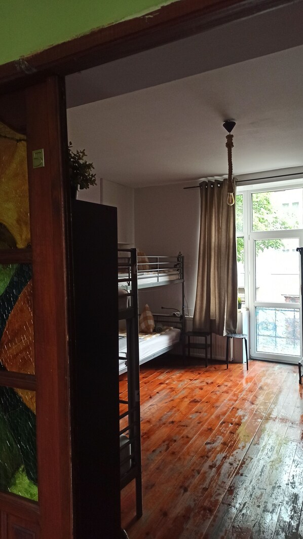 A room with a bunk bed, a wooden floor, a window with curtains, and a plant on a table.