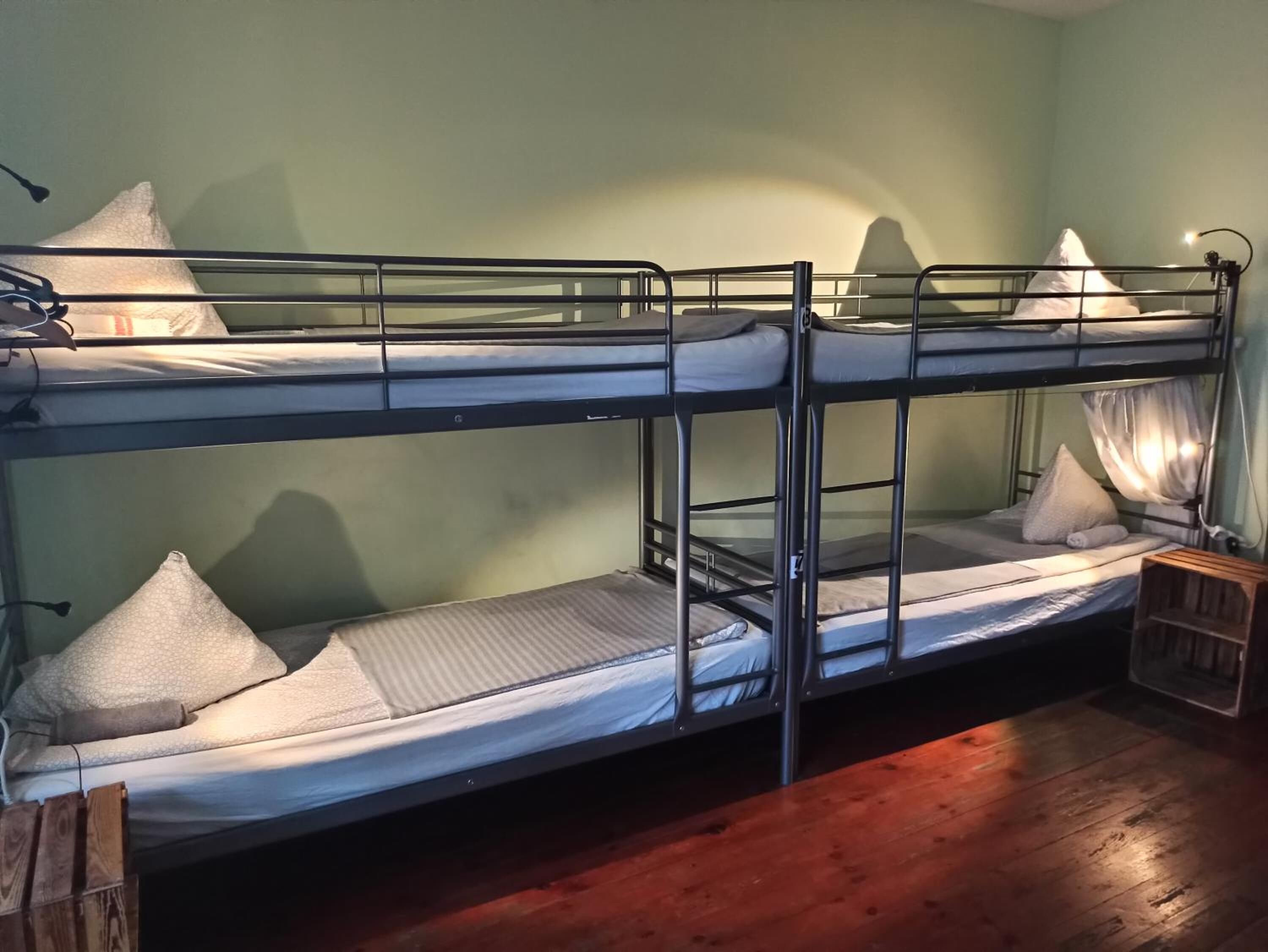 Habitación con literas, suelo de madera y una mesita de noche pequeña.