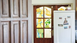 Una cocina con un refrigerador blanco, una puerta de madera con vidrieras y una pequeña planta en maceta encima.