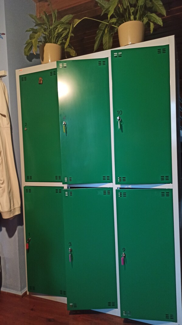 A row of green lockers with numbers 1 to 10, a beige coat hanging on the left, and a potted plant on top.