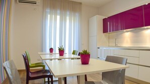 A modern kitchen with white cabinets, a white countertop, and a purple upper cabinet. There are two chairs and a table with potted plants. - Mare di Luci (Salerno)