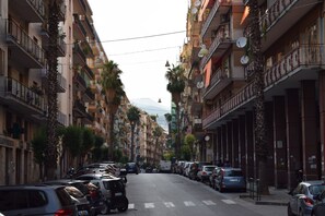 A street lined with multi-story buildings, parked cars, and palm trees. - Mare di Luci (Salerno)