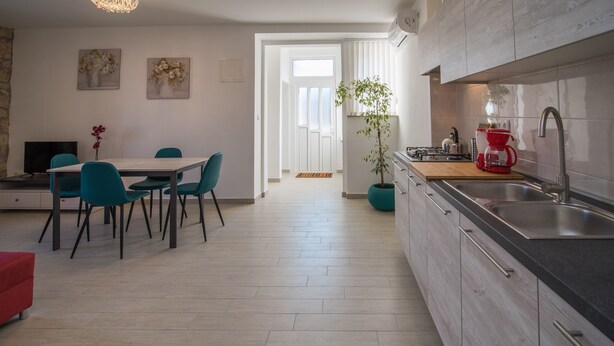 A modern kitchen with a sink, stove, and red coffee maker. There is a dining area with a table and chairs, and a potted plant. - Apartment for 4 person (Vrbnik)