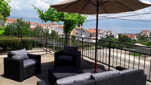 A balcony with wicker furniture, a large umbrella, and a view of houses and a body of water. - Apartment for 4 person (Vrbnik)