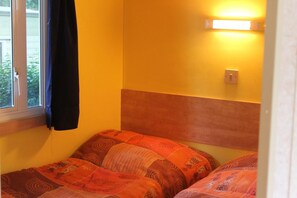 A room with a bed, a window with a curtain, and a wall-mounted light fixture. - Camping du Pré Coulet (Saint-Pierreville)