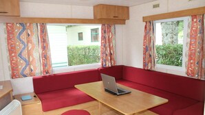 Un espacio habitable compacto con un sofá rojo, una mesa de madera con una computadora portátil y un taburete pequeño.