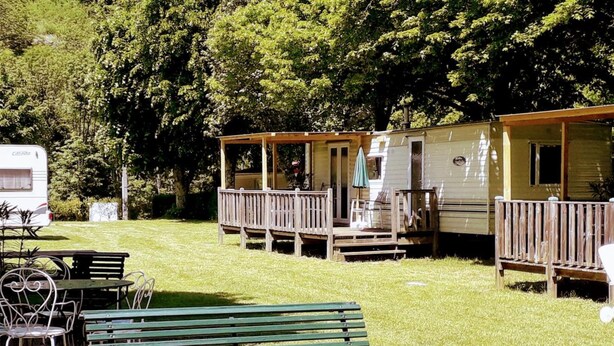 Un camping con un banco verde, mesas de picnic y una zona cubierta con terraza.