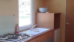 Una cocina compacta con estufa a gas, un lavamanos y un ventanal que deja entrar luz natural.