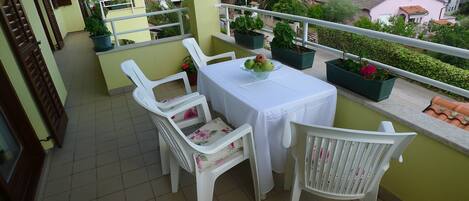 A balcony with white plastic chairs and a table, potted plants, and a view of the surrounding neighborhood.