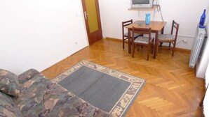A room with a wooden floor, a sofa, a dining table with chairs, a television on a stand, and a radiator. - Holiday Apartment Near the Beach for 4 Persons With one Bedroom (Medulin)