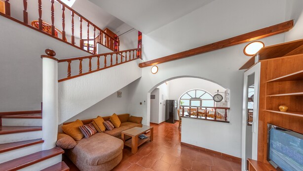 A spacious living area with a staircase, a sofa set, a coffee table, and a TV on a wooden stand.