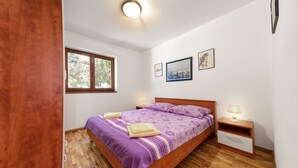 A bedroom with a wooden bed, a window, a nightstand, and a wall-mounted lamp.
