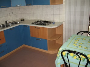 Compact kitchen with gas stove, stainless steel sink, and dining area.