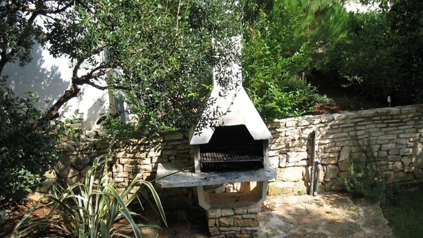 A stone barbecue grill with a chimney, surrounded by a stone wall and greenery. - Six Person Apartment With 2 Bedrooms Near the Beach in Pjescana Uvala (Medulin)