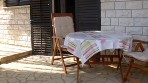 A patio with a table and chairs, a stone floor, and a building with a brick wall and shutters. - Apartment for two Persons With Swimming Pool Near the Beach (Medulin)