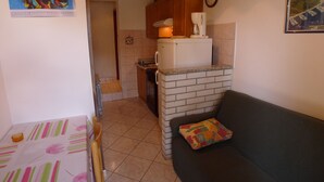 A compact living space with a kitchenette, a dining area, and a sofa with a cushion. - Apartment for two Persons With Swimming Pool Near the Beach (Medulin)