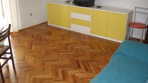 A room with a wooden parquet floor, a yellow and white cabinet with a television on top, a blue sofa, and a red stool. - Six Person Apartment With 2 Bedrooms Near the Beach in Pjescana Uvala (Medulin)
