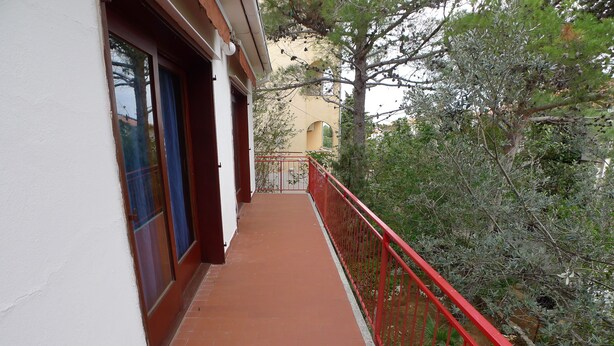 A narrow balcony with red railings, a tiled floor, and a view of surrounding trees and buildings. - Apartment for six Persons With Three Bedrooms and Internet (Medulin)