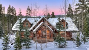 A log cabin with a symmetrical roof and multiple chimneys, surrounded by snow-covered ground and trees. - Highlands Treehouse with Shuffleboard & Private Hot Tub! Golf Course & Mountain Views! (Breckenridge)