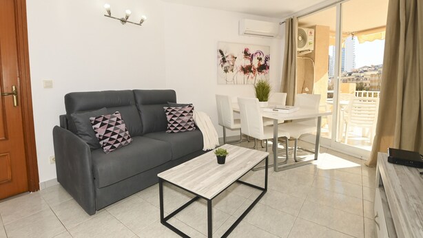 Un salon moderne avec un canapé gris, une table basse blanche et un coin repas comprenant une table et des chaises blanches.