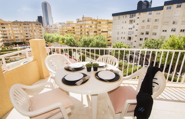 Ein Balkon mit einem runden Tisch, gedeckt für vier Personen, umgeben von weißen Plastikstühlen mit Kissen.