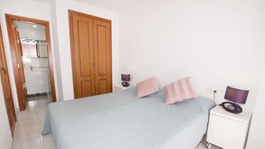Une chambre à coucher avec un lit, deux tables de chevet, une armoire et une salle de bain visible à travers une porte ouverte.
