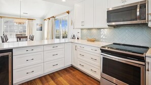 Une cuisine moderne avec des meubles blancs, un four à micro-ondes en acier inoxydable et une cuisinière noire.