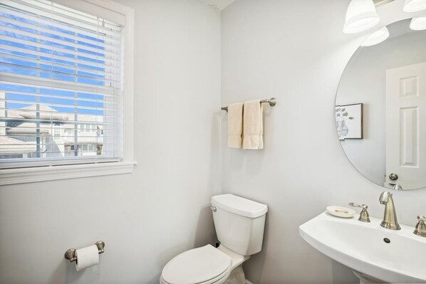 Et badeværelse med toilet, vask og et vindue med persienner.