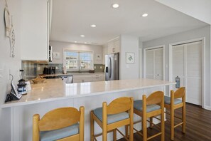 A modern kitchen with a central island, bar stools, and a refrigerator.