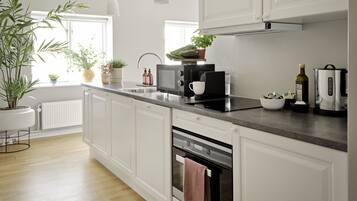 Una cocina moderna con armarios blancos, encimera de acero inoxidable, horno empotrado y ventana que deja entrar luz natural.