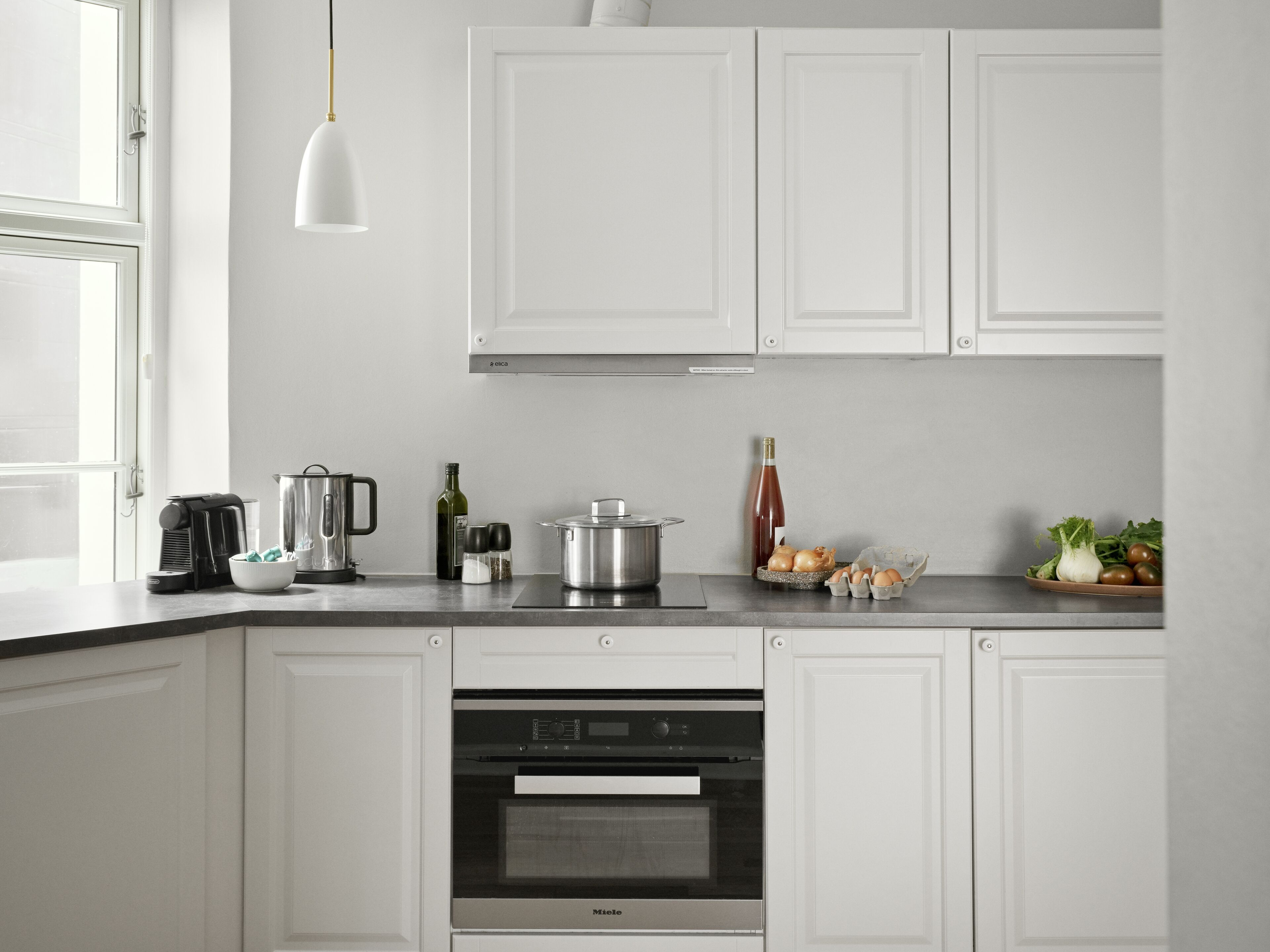 A modern kitchen with white cabinets, a built-in oven, a coffee maker, and various kitchen items on the counter.