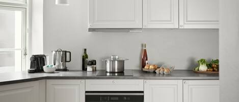 A modern kitchen with white cabinets, a built-in oven, a coffee maker, and various kitchen items on the counter.