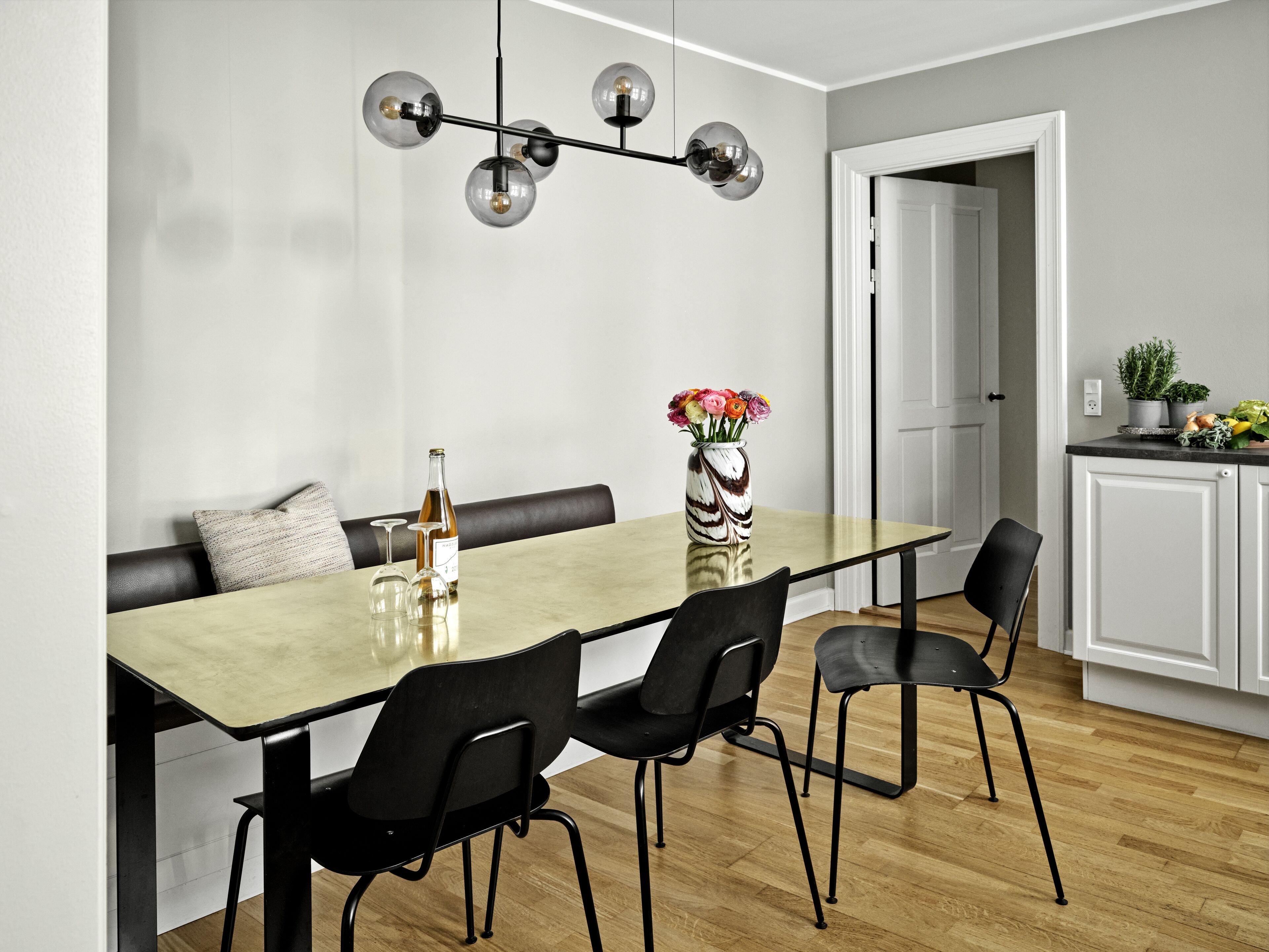 A dining area with a long table, black chairs, a vase with flowers, and a bottle of wine.