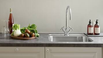 A kitchen with a stainless steel sink, a bowl of vegetables, a wine bottle, and two bottles of hand soap.