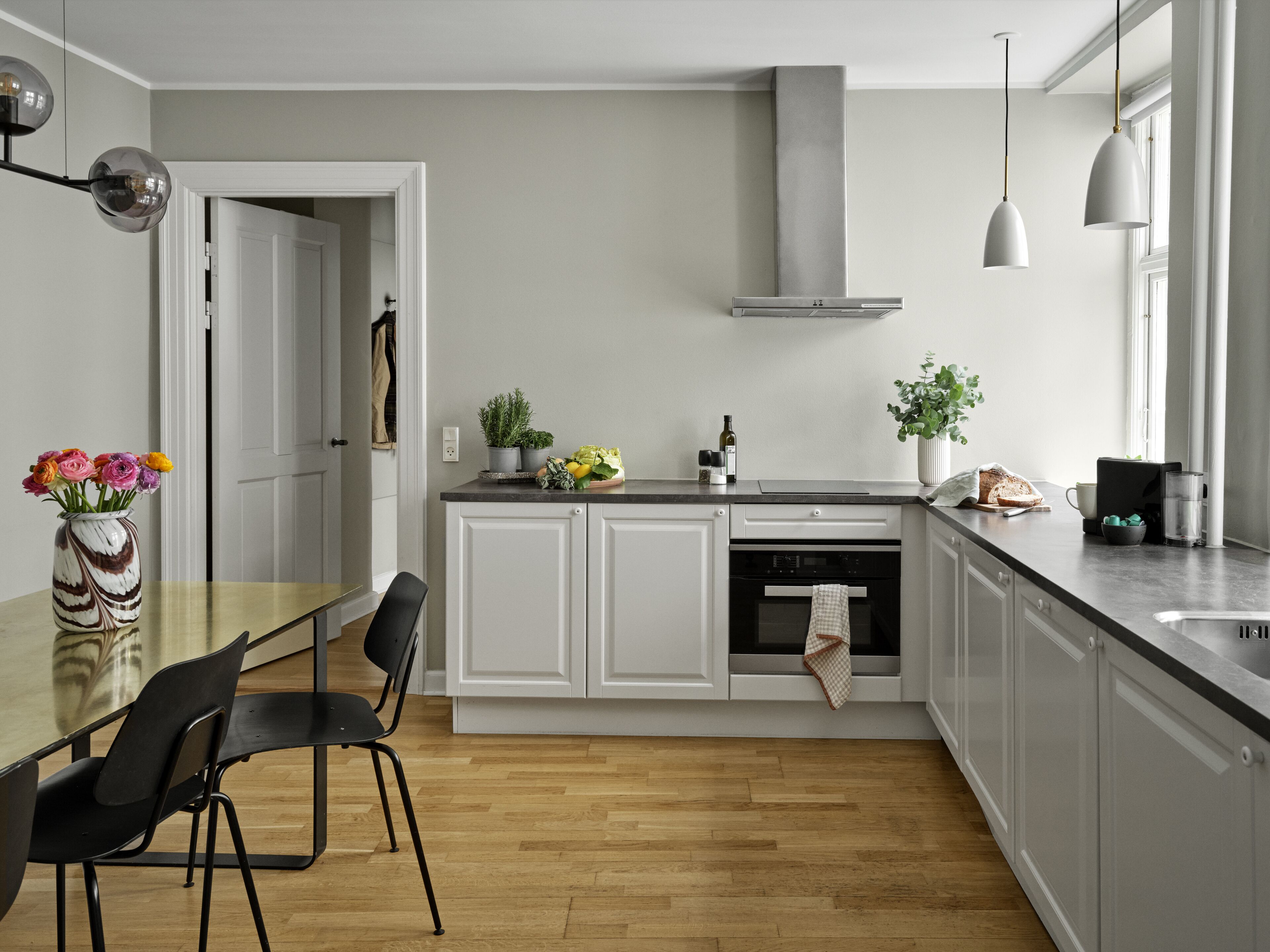 A modern kitchen with white cabinets, a wooden floor, a dining table with chairs, and pendant lighting.