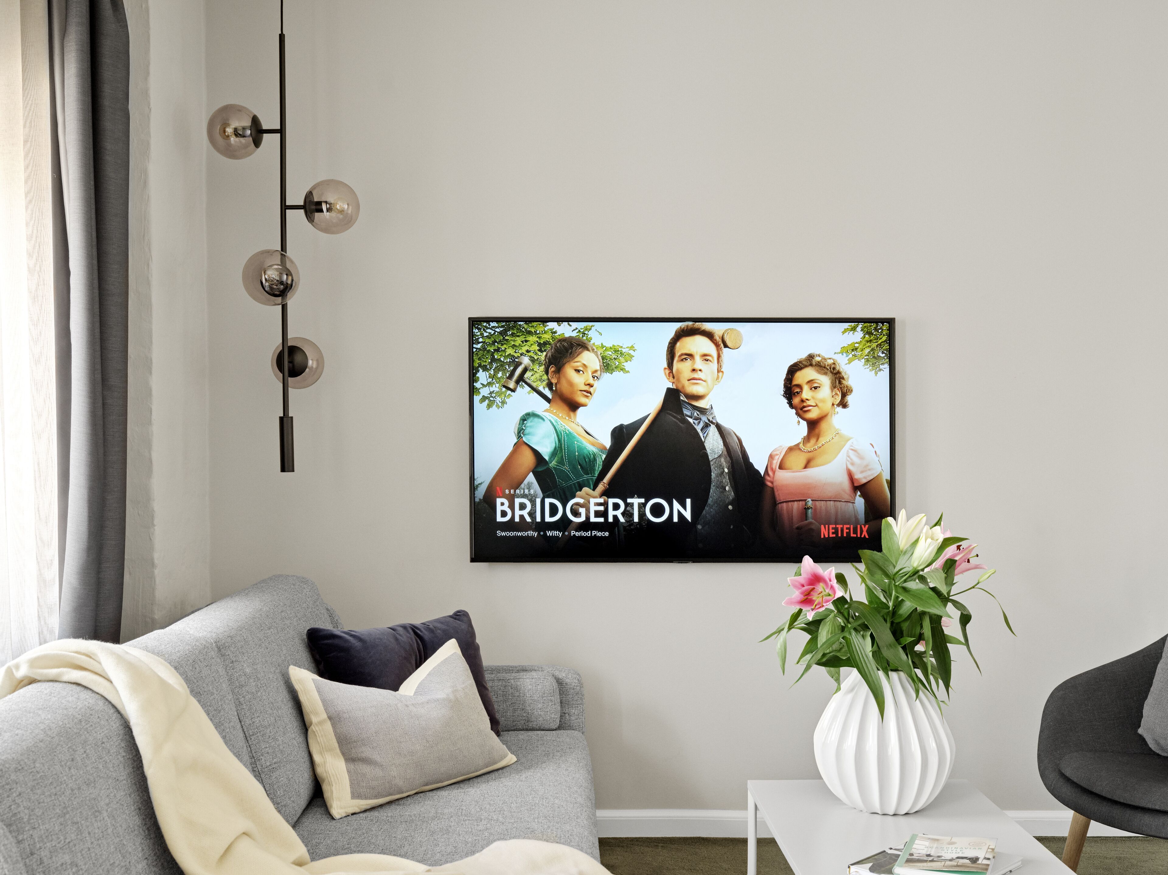 Un salon avec un canapé gris, une table basse blanche et un téléviseur encadré diffusant la série « Bridgerton » de Netflix.
