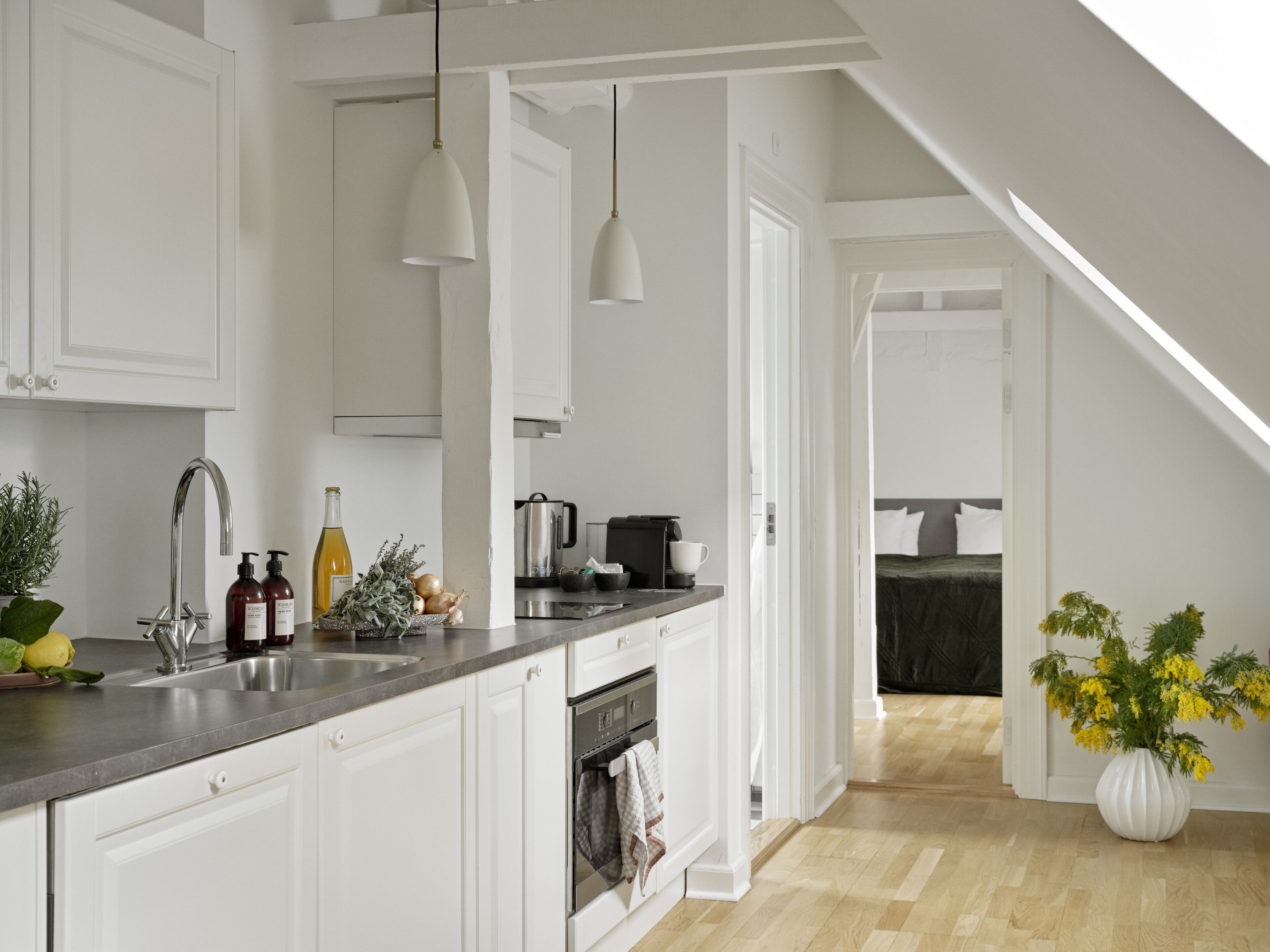 Une cuisine moderne avec des meubles blancs, un évier en acier inoxydable et des luminaires suspendus.