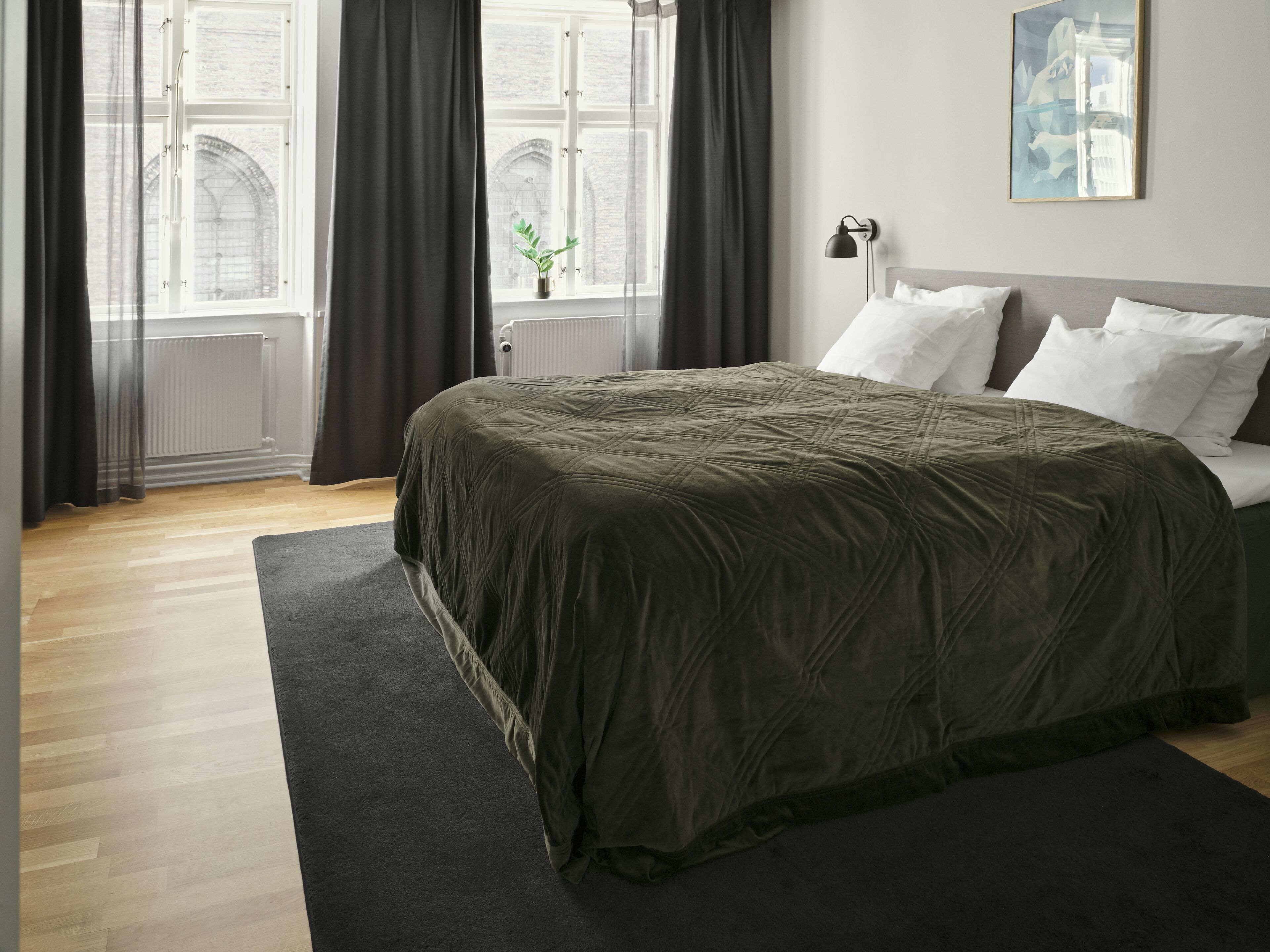 A bedroom with a large bed, dark curtains, a radiator, and a window with a view of a building.