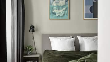 A bedroom with a bed, pillows, a nightstand with a lamp, a plant, and two framed artworks on the wall.
