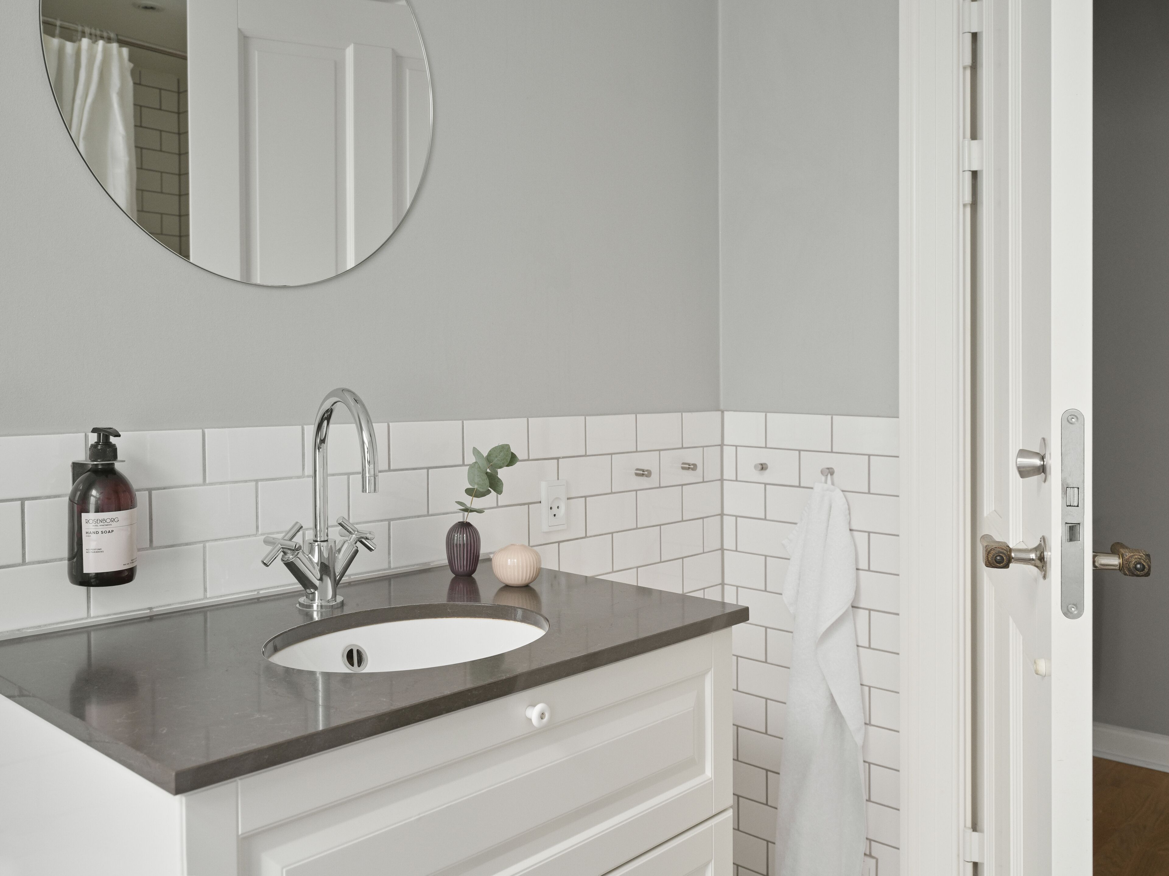 A bathroom with a white sink, a mirror, and a towel hanging on the door.