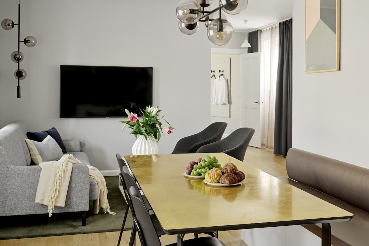Un salon moderne avec une table à manger, un canapé gris et un téléviseur fixé au mur.