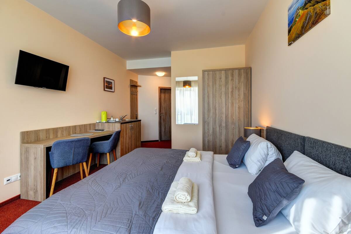 A hotel room with a large bed, a desk with two chairs, a television, and a painting on the wall.