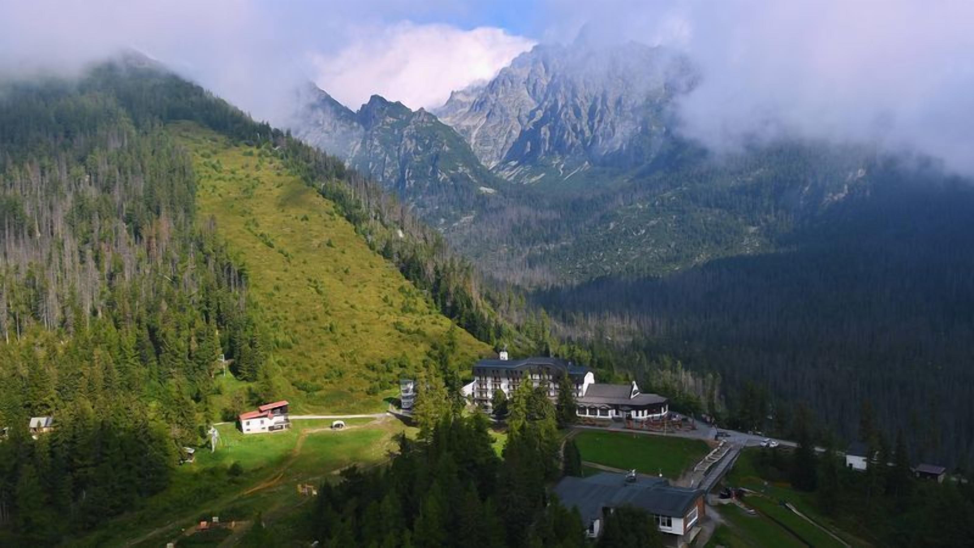 A mountain lodge with a large building and smaller structures, surrounded by dense forest and mountains.