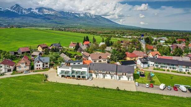 A residential area with houses, a large building, and a mountain range in the background. - Penzión Čerešnový Sad (Mengusovce)